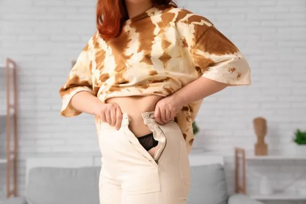 Image of woman trying to do her trousers up after pregnancy weight gain Northamptonshire